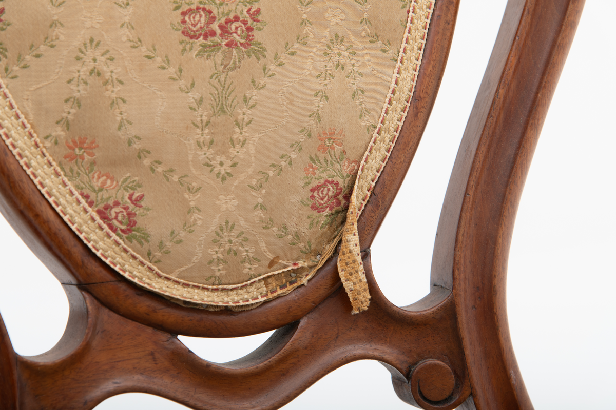 Gruppe med sofa, to lenestoler og tre mindre stoler uten armlener i stilen nyrokokko. Gyllengult trekk med rosemotiv og mørkt treverk med buede, organiske linjer.
