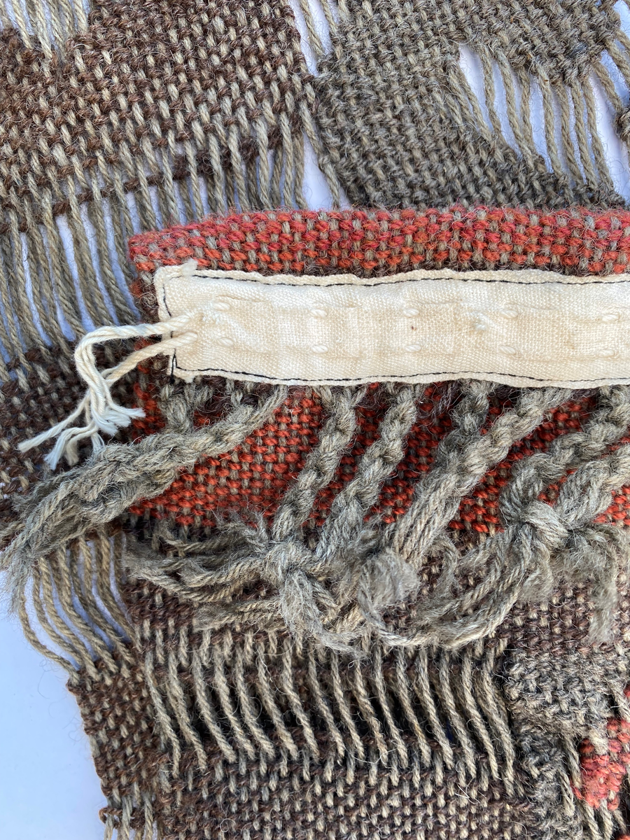 Gardin, vevd i bruntoner og med et dekorelementer i rød og mørkere brun. Rød kant øverst med et bånd på baksiden. Frynser langs nedre kant. Fargene er delvis bleket i striper på baksiden. Gardinen er i samme teknikk og med samme mønster som to andre gardiner, en løper og et putetrekk. (Se relaterte objekter)