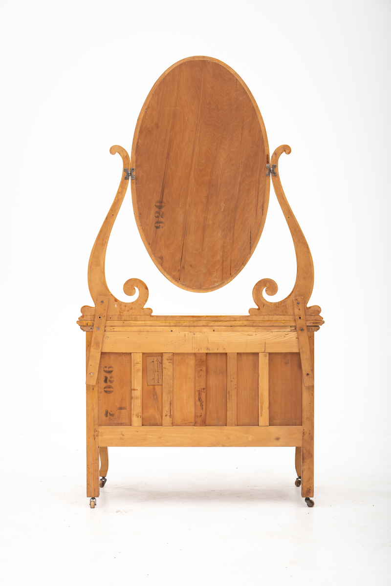 Kommode. Topplate og fronten på kommoden er bølget i formen. To mindre skuffer øverst, og en stor låsbar skuff nederst. Treknotter. Ben med hjul.