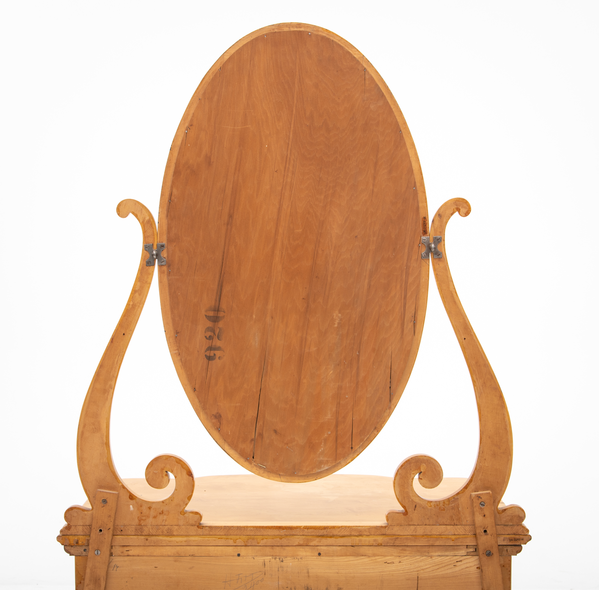 Ovalt speil i ramme. Speilet er festet til et stativ i hver side. Sidestykkene på stativet har S-form og utskjæringer og er festet til en fotlist. Denne fotlisten festes på toppen av kommoden.