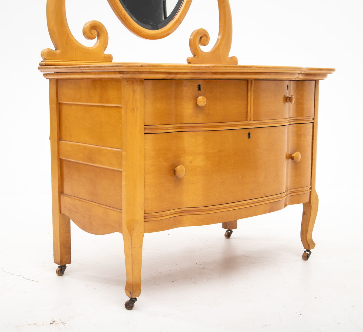 Kommode. Topplate og fronten på kommoden er bølget i formen. To mindre skuffer øverst, og en stor låsbar skuff nederst. Treknotter. Ben med hjul.