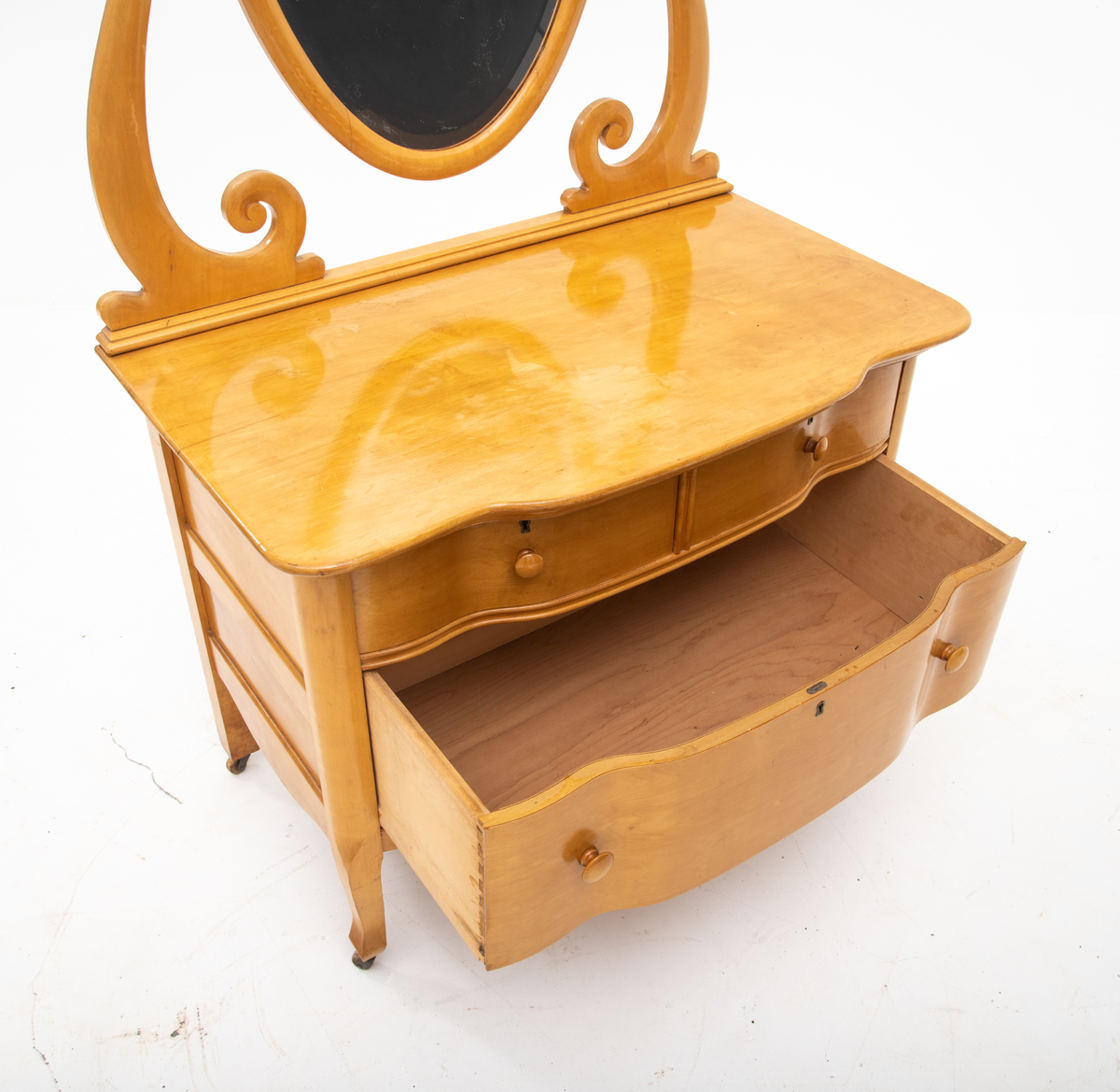 Kommode. Topplate og fronten på kommoden er bølget i formen. To mindre skuffer øverst, og en stor låsbar skuff nederst. Treknotter. Ben med hjul.