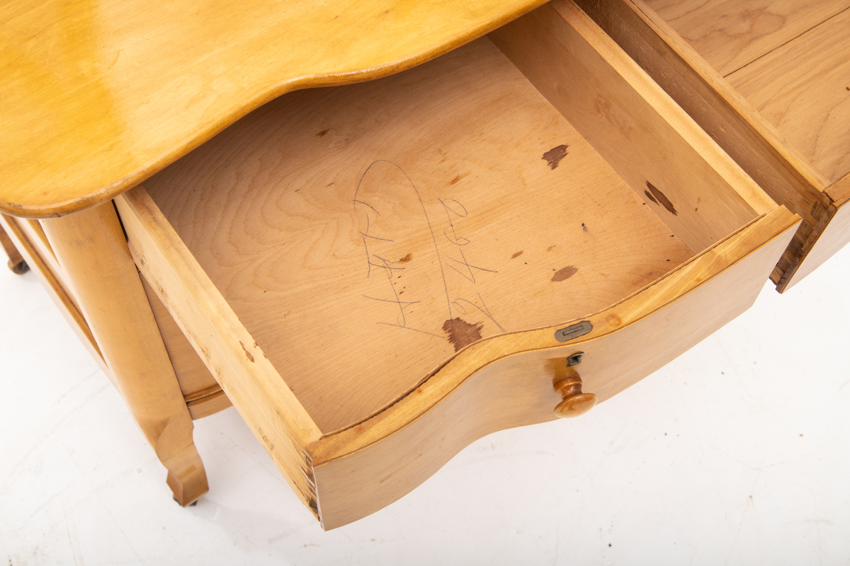 Kommode. Topplate og fronten på kommoden er bølget i formen. To mindre skuffer øverst, og en stor låsbar skuff nederst. Treknotter. Ben med hjul.