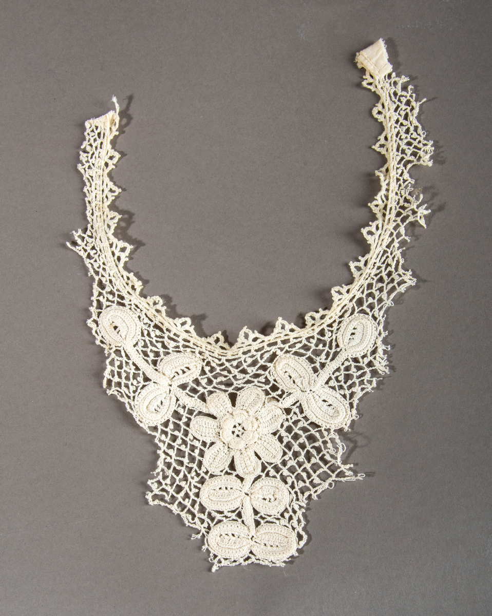 Blondekrage/kjolepynt. Ekryfarget. Motiv midt foran av en blomst med stilk og blader.