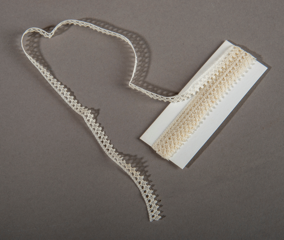 Blonderemse. Hvit. Smal. "Hullkant" langs den ene siden, taggete langs den andre.