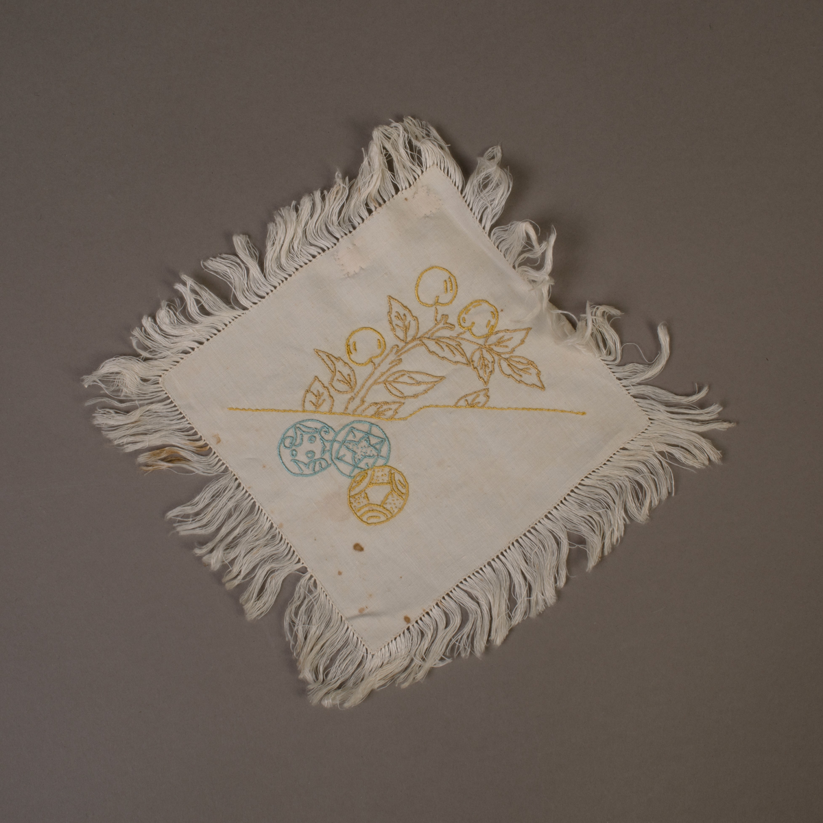 En av tolv tallerkendempere. Kvadratiske med frynser rundt det hele. Broderte med forskjellig japanske motiver.