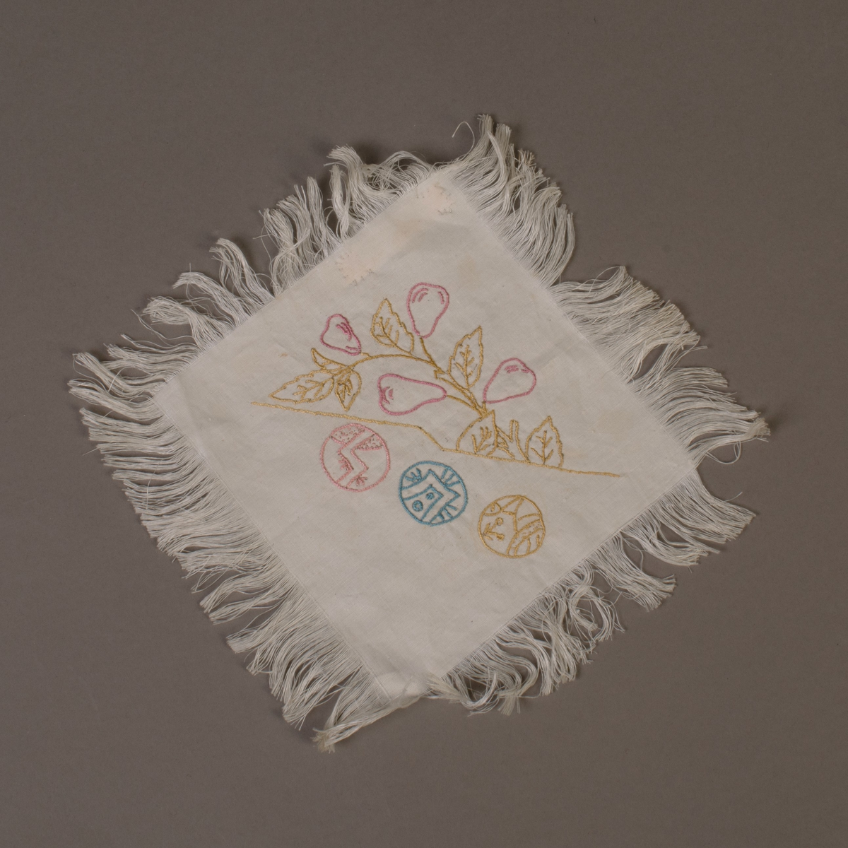 En av tolv tallerkendempere. Kvadratiske med frynser rundt det hele. Broderte med forskjellig japanske motiver.
