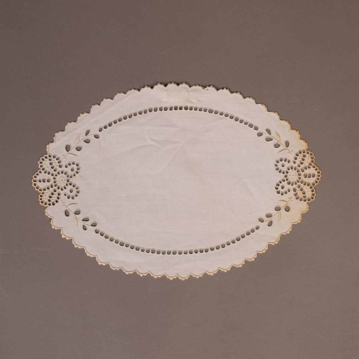 Oval brikke med engelsk broderi med tungekant. To store roser med blad. Fra ca. 1900.