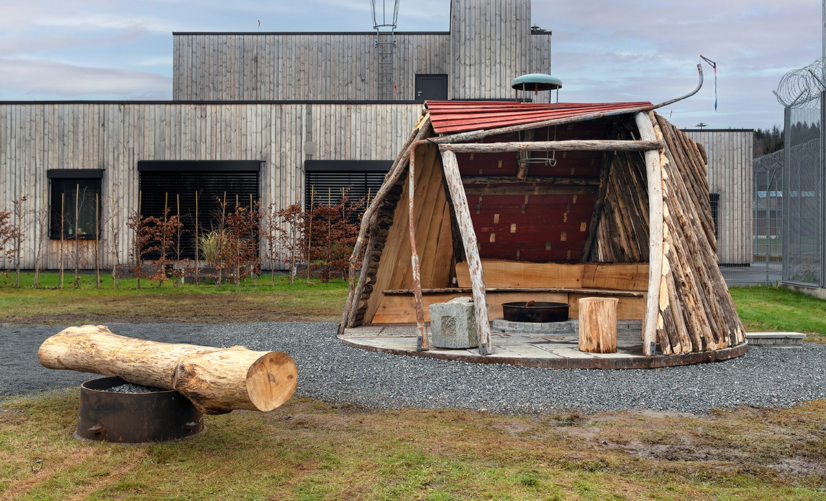 Tekst på nordsamisk lenger ned / Geahca sámegiela teavstta vuolábealde

"Flukthus/Báhtarangoahti" er et kunstverk utført av Vuogas, arkitekturkollektivet med kunstnerne og arkitektene Joar Nango og Eystein Talleraas, i nært samarbeid med innsatte og ansatte ved Ila. Verket har formen og funksjonen til en gamme, men er ikke bygget helt slik en gamme tradisjonelt blir bygget. Hovedstrukturen og de bærende elementene er tilvirket og satt sammen på tradisjonelt vis, men uten jord, torv og never slik det samiske folket gjennom tidene har benyttet seg av. Som vanlig når Vuogas engasjeres i prosjekter, har de undersøkt, funnet og brukt lokale materialer som bærer med seg historikken fra stedet. I dette tilfellet trevirke fra skogen rundt Ila, i tillegg til funnet materiale og gjenstander fra fengselet og gartneriets område. "Flukthus/Báhtarangoahti" er et arkitektonisk kunstverk, men også et oppholdssted og et sosialt rom. Det er bygget for avdelingen, med tanke for de innsatte og ansatte ved NFFA, og der intensjonen har vært at gammen og bålplassen skal bli et godt sted å være.

Joar Nango (f. 1979) er en samisk-norsk kunstner og arkitekt som bor og jobber i Tromsø. Han er utdannet arkitekt fra NTNU i Trondheim og grunnlegger av arkitekturkollektivet Vuogas sammen med Eystein Talleraas (f. 1980). Talleraas bor og jobber i Oslo, og er utdannet arkitekt fra NTNU i Trondheim.

"Báhtarangoahti/Flukthus" lea dáiddadagus, man Vuogas, dáiddára ja arkiteavtta guoktá Joar Nango ja Eystein Talleraas arkitektuvrakollektiiva lea ráhkadan, lagas ovttasbarggus Ila giddagasa fá¿ggaiguin ja virggehasaiguin.  Dáiddadahkosis lea goadi hápmi ja doaibma, muhto dat ii leat huksejuvvon jur dego goahti árbevirolaccat huksejuvvo. Riggi ja válddahagat leat ávdnejuvvon ja cohkkejuvvon árbevirolaš vuogi mielde, muhto goadis eai leat lavnnjit, darffit ja beassit, maid sápmelaccat áiggiid cada leat geavahan godiineaset. Nugo dábálaccat go Vuogas bálkáhuvvo prošeavttaide, de lea arkiteaktakollektiiva guorahallan, gávdnan ja geavahan báikkálaš ávdnasiid, main lea lagasbirrasa historihkka. Dán oktavuodas lea ávnnasmuorat vižžojuvvon vuovddis Ila birra, ja lassin leat gávdnon ávdnasat ja biergasat giddagasas ja gilvvagárdedoalu guovllus. "Báhtarangoahti/Flukthus" lea arkitektuvrralaš dáiddadagus, muhto maiddái orostallansadji ja servvoštallanlatnja. Dat lea huksejuvvon ossodaga várás, NFFA [našuvnnalaš nannejuvvon oktasašossodaga] fá¿ggaid ja virggehasaid gorrái, ja man áigumuš  lea leamaš ahte goahti ja árran galget šaddat sadjin gos lea vuogas leahkit.

Joar Nango (r. 1979) lea Norgga beali sámi dáiddár ja arkiteakta, gii ássá ja bargá Romssas. Son lea oahppan arkiteaktan NTNU:s [Norgga teknihkalaš-luonddudiedalaš universiteahtas] Tråantes/Troanddimis, ja lea vuoddudan Vuogas arkitektuvrakollektiivva ovttas Eystein Talleraas:in (r. 1980). Talleraas ássá ja bargá Osloves, ja lea oahppan arkiteaktan NTNU:s Tråantes/Troanddimis.