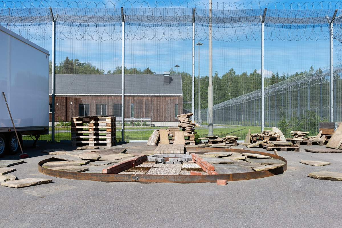 Tekst på nordsamisk lenger ned / Geahca sámegiela teavstta vuolábealde

"Flukthus/Báhtarangoahti" er et kunstverk utført av Vuogas, arkitekturkollektivet med kunstnerne og arkitektene Joar Nango og Eystein Talleraas, i nært samarbeid med innsatte og ansatte ved Ila. Verket har formen og funksjonen til en gamme, men er ikke bygget helt slik en gamme tradisjonelt blir bygget. Hovedstrukturen og de bærende elementene er tilvirket og satt sammen på tradisjonelt vis, men uten jord, torv og never slik det samiske folket gjennom tidene har benyttet seg av. Som vanlig når Vuogas engasjeres i prosjekter, har de undersøkt, funnet og brukt lokale materialer som bærer med seg historikken fra stedet. I dette tilfellet trevirke fra skogen rundt Ila, i tillegg til funnet materiale og gjenstander fra fengselet og gartneriets område. "Flukthus/Báhtarangoahti" er et arkitektonisk kunstverk, men også et oppholdssted og et sosialt rom. Det er bygget for avdelingen, med tanke for de innsatte og ansatte ved NFFA, og der intensjonen har vært at gammen og bålplassen skal bli et godt sted å være.

Joar Nango (f. 1979) er en samisk-norsk kunstner og arkitekt som bor og jobber i Tromsø. Han er utdannet arkitekt fra NTNU i Trondheim og grunnlegger av arkitekturkollektivet Vuogas sammen med Eystein Talleraas (f. 1980). Talleraas bor og jobber i Oslo, og er utdannet arkitekt fra NTNU i Trondheim.

"Báhtarangoahti/Flukthus" lea dáiddadagus, man Vuogas, dáiddára ja arkiteavtta guoktá Joar Nango ja Eystein Talleraas arkitektuvrakollektiiva lea ráhkadan, lagas ovttasbarggus Ila giddagasa fá¿ggaiguin ja virggehasaiguin.  Dáiddadahkosis lea goadi hápmi ja doaibma, muhto dat ii leat huksejuvvon jur dego goahti árbevirolaccat huksejuvvo. Riggi ja válddahagat leat ávdnejuvvon ja cohkkejuvvon árbevirolaš vuogi mielde, muhto goadis eai leat lavnnjit, darffit ja beassit, maid sápmelaccat áiggiid cada leat geavahan godiineaset. Nugo dábálaccat go Vuogas bálkáhuvvo prošeavttaide, de lea arkiteaktakollektiiva guorahallan, gávdnan ja geavahan báikkálaš ávdnasiid, main lea lagasbirrasa historihkka. Dán oktavuodas lea ávnnasmuorat vižžojuvvon vuovddis Ila birra, ja lassin leat gávdnon ávdnasat ja biergasat giddagasas ja gilvvagárdedoalu guovllus. "Báhtarangoahti/Flukthus" lea arkitektuvrralaš dáiddadagus, muhto maiddái orostallansadji ja servvoštallanlatnja. Dat lea huksejuvvon ossodaga várás, NFFA [našuvnnalaš nannejuvvon oktasašossodaga] fá¿ggaid ja virggehasaid gorrái, ja man áigumuš  lea leamaš ahte goahti ja árran galget šaddat sadjin gos lea vuogas leahkit.

Joar Nango (r. 1979) lea Norgga beali sámi dáiddár ja arkiteakta, gii ássá ja bargá Romssas. Son lea oahppan arkiteaktan NTNU:s [Norgga teknihkalaš-luonddudiedalaš universiteahtas] Tråantes/Troanddimis, ja lea vuoddudan Vuogas arkitektuvrakollektiivva ovttas Eystein Talleraas:in (r. 1980). Talleraas ássá ja bargá Osloves, ja lea oahppan arkiteaktan NTNU:s Tråantes/Troanddimis.