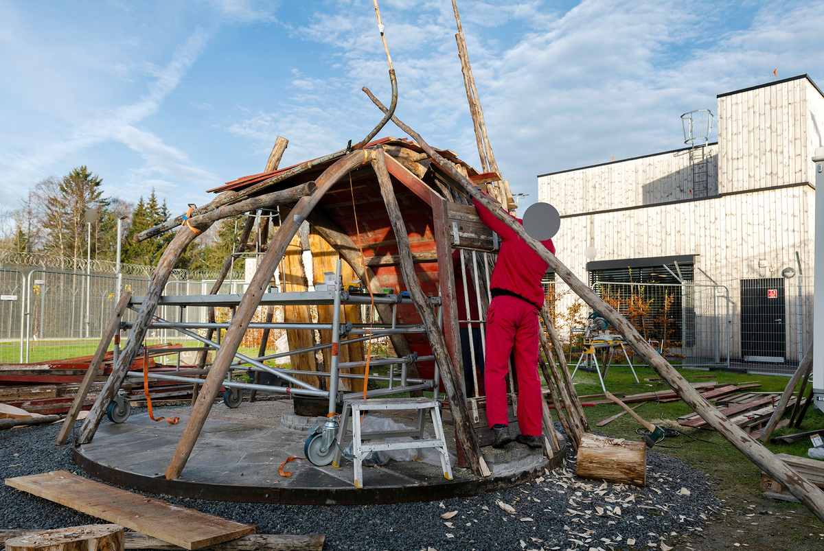 Tekst på nordsamisk lenger ned / Geahca sámegiela teavstta vuolábealde

"Flukthus/Báhtarangoahti" er et kunstverk utført av Vuogas, arkitekturkollektivet med kunstnerne og arkitektene Joar Nango og Eystein Talleraas, i nært samarbeid med innsatte og ansatte ved Ila. Verket har formen og funksjonen til en gamme, men er ikke bygget helt slik en gamme tradisjonelt blir bygget. Hovedstrukturen og de bærende elementene er tilvirket og satt sammen på tradisjonelt vis, men uten jord, torv og never slik det samiske folket gjennom tidene har benyttet seg av. Som vanlig når Vuogas engasjeres i prosjekter, har de undersøkt, funnet og brukt lokale materialer som bærer med seg historikken fra stedet. I dette tilfellet trevirke fra skogen rundt Ila, i tillegg til funnet materiale og gjenstander fra fengselet og gartneriets område. "Flukthus/Báhtarangoahti" er et arkitektonisk kunstverk, men også et oppholdssted og et sosialt rom. Det er bygget for avdelingen, med tanke for de innsatte og ansatte ved NFFA, og der intensjonen har vært at gammen og bålplassen skal bli et godt sted å være.

Joar Nango (f. 1979) er en samisk-norsk kunstner og arkitekt som bor og jobber i Tromsø. Han er utdannet arkitekt fra NTNU i Trondheim og grunnlegger av arkitekturkollektivet Vuogas sammen med Eystein Talleraas (f. 1980). Talleraas bor og jobber i Oslo, og er utdannet arkitekt fra NTNU i Trondheim.

"Báhtarangoahti/Flukthus" lea dáiddadagus, man Vuogas, dáiddára ja arkiteavtta guoktá Joar Nango ja Eystein Talleraas arkitektuvrakollektiiva lea ráhkadan, lagas ovttasbarggus Ila giddagasa fá¿ggaiguin ja virggehasaiguin.  Dáiddadahkosis lea goadi hápmi ja doaibma, muhto dat ii leat huksejuvvon jur dego goahti árbevirolaccat huksejuvvo. Riggi ja válddahagat leat ávdnejuvvon ja cohkkejuvvon árbevirolaš vuogi mielde, muhto goadis eai leat lavnnjit, darffit ja beassit, maid sápmelaccat áiggiid cada leat geavahan godiineaset. Nugo dábálaccat go Vuogas bálkáhuvvo prošeavttaide, de lea arkiteaktakollektiiva guorahallan, gávdnan ja geavahan báikkálaš ávdnasiid, main lea lagasbirrasa historihkka. Dán oktavuodas lea ávnnasmuorat vižžojuvvon vuovddis Ila birra, ja lassin leat gávdnon ávdnasat ja biergasat giddagasas ja gilvvagárdedoalu guovllus. "Báhtarangoahti/Flukthus" lea arkitektuvrralaš dáiddadagus, muhto maiddái orostallansadji ja servvoštallanlatnja. Dat lea huksejuvvon ossodaga várás, NFFA [našuvnnalaš nannejuvvon oktasašossodaga] fá¿ggaid ja virggehasaid gorrái, ja man áigumuš  lea leamaš ahte goahti ja árran galget šaddat sadjin gos lea vuogas leahkit.

Joar Nango (r. 1979) lea Norgga beali sámi dáiddár ja arkiteakta, gii ássá ja bargá Romssas. Son lea oahppan arkiteaktan NTNU:s [Norgga teknihkalaš-luonddudiedalaš universiteahtas] Tråantes/Troanddimis, ja lea vuoddudan Vuogas arkitektuvrakollektiivva ovttas Eystein Talleraas:in (r. 1980). Talleraas ássá ja bargá Osloves, ja lea oahppan arkiteaktan NTNU:s Tråantes/Troanddimis.