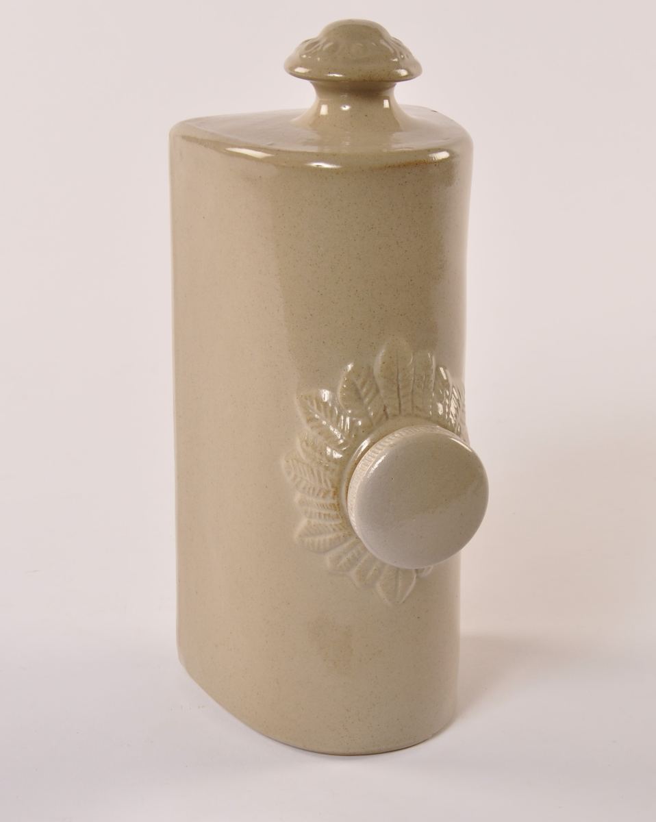 Varmeflaske av gråglassert keramikk, sylinder med flat bunn. Håndtak i ene kortenden og skrukork midt på toppen med enkel bladekor rundt.