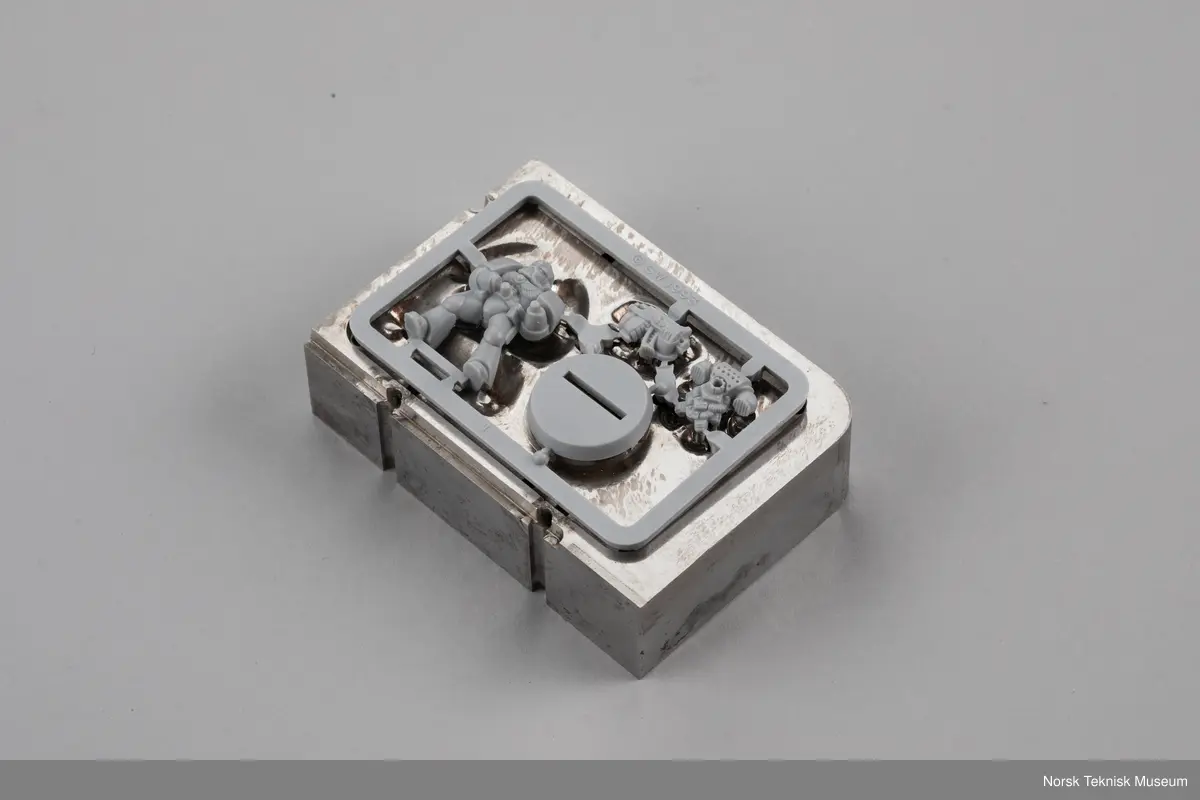 Dette er 2 eldre "Space marine" modeller som brukes i spillet Warhammer 40,000. Figuren ble gitt som gave til museet i forbindelse med utstillingen "Modeller og Miniatyrer" i 2024. Den ene modellen er satt sammen og den andre er fortsatt på støperamme. Støperammen til den sammensatte figuren er en del av gjenstanden.

Den avbildede støpeformen er original men er ikke en del av gjenstanden. Den var et innlån fra produsent ved aksesjon.