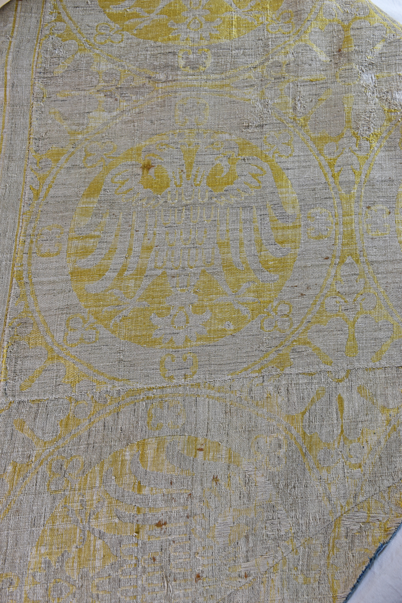 Mässhaken är vävd i s.k. Regensburg-brokad. Dubbelt varpsystem med lin och silke, botteninslag av silke samt mönsterinslag av tarmguld spunnet runt en lintråd. (Taquete alt. samitum)
Tarmguldet är idag bortnött.

Mönstret i form av dubbelörnar inom cirklar har stark anknytning till italiensk-bysantinska mönster. 

Enligt A. Geijer tillverkad i Spanien eller Tyskland.

Litteratur: Medeltida vävnader och broderier i Sverige.
av A. Branting och A. Lindblom. del II, plansch 217, text sid 101 ff.
"Ur Textilkonstens historia", Agnes Geijer. 1972. (sid 162, pl 34 a.)