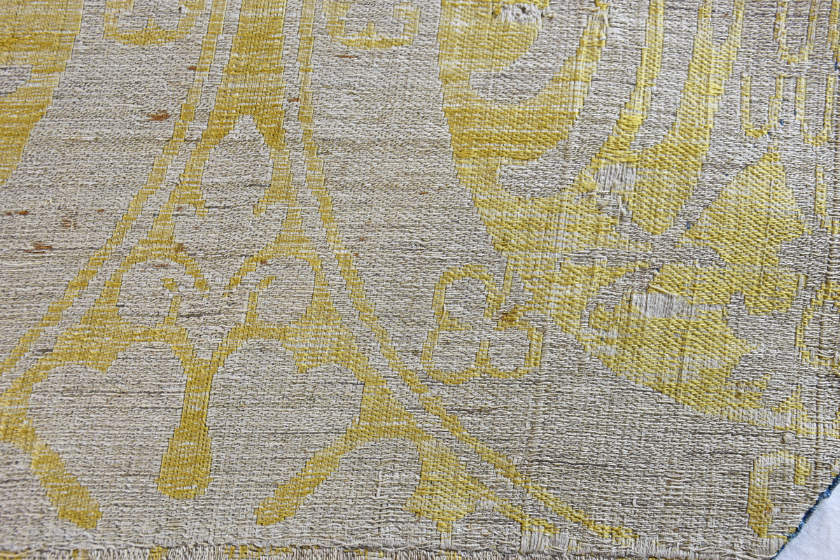 Mässhaken är vävd i s.k. Regensburg-brokad. Dubbelt varpsystem med lin och silke, botteninslag av silke samt mönsterinslag av tarmguld spunnet runt en lintråd. (Taquete alt. samitum)
Tarmguldet är idag bortnött.

Mönstret i form av dubbelörnar inom cirklar har stark anknytning till italiensk-bysantinska mönster. 

Enligt A. Geijer tillverkad i Spanien eller Tyskland.

Litteratur: Medeltida vävnader och broderier i Sverige.
av A. Branting och A. Lindblom. del II, plansch 217, text sid 101 ff.
"Ur Textilkonstens historia", Agnes Geijer. 1972. (sid 162, pl 34 a.)