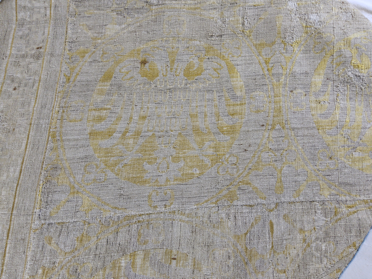 Mässhaken är vävd i s.k. Regensburg-brokad. Dubbelt varpsystem med lin och silke, botteninslag av silke samt mönsterinslag av tarmguld spunnet runt en lintråd. (Taquete alt. samitum)
Tarmguldet är idag bortnött.

Mönstret i form av dubbelörnar inom cirklar har stark anknytning till italiensk-bysantinska mönster. 

Enligt A. Geijer tillverkad i Spanien eller Tyskland.

Litteratur: Medeltida vävnader och broderier i Sverige.
av A. Branting och A. Lindblom. del II, plansch 217, text sid 101 ff.
"Ur Textilkonstens historia", Agnes Geijer. 1972. (sid 162, pl 34 a.)