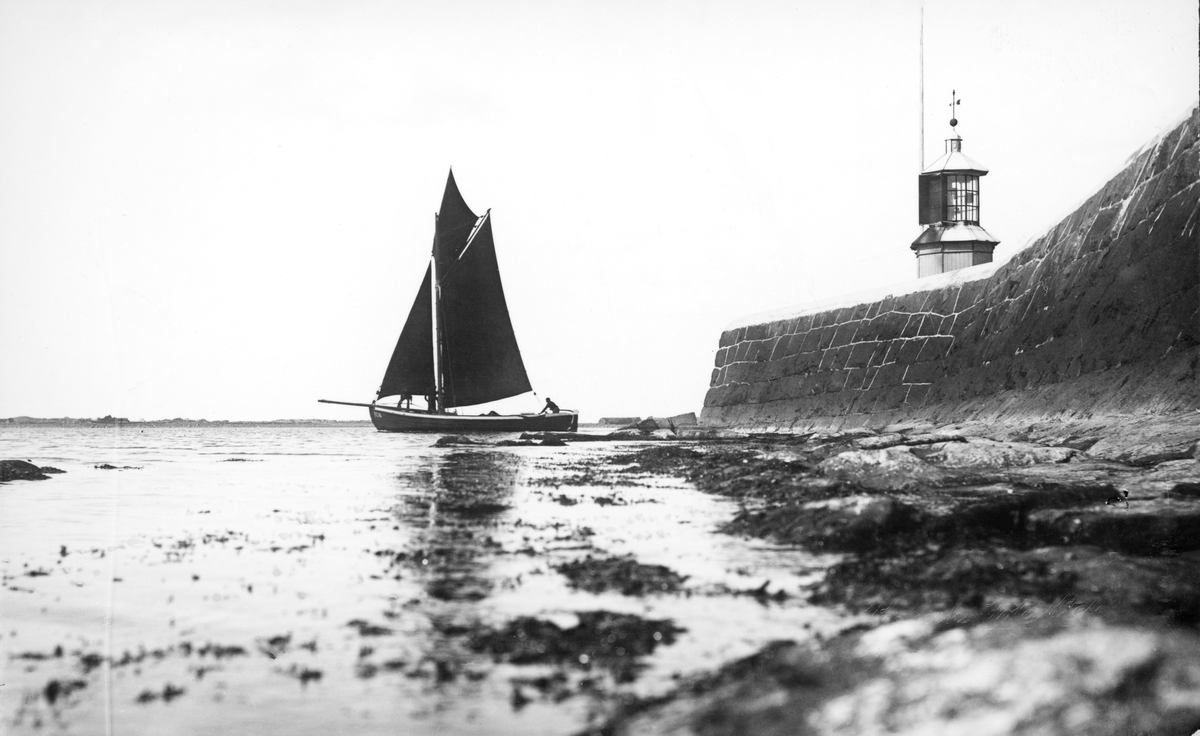 Kolorerat vykort, "Hamnpiren. Warberg." Piren med fyren och en segelbåt på väg ut ur hamnen. Bild 2 är svartvit och högupplöst.