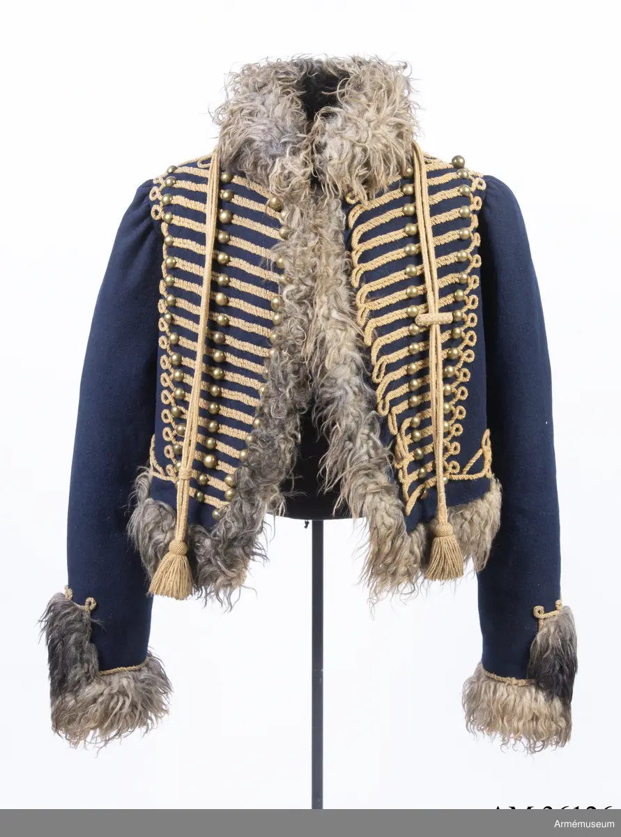 Blå päls med krage och ärmuppslag av gråbrunt fårskinn, med snören av gult ullgarn.

Pälsen är sydd av mörkblått kläde och är helfodrad med vitt, numera gulnat, korthårigt fårskinn. Ärmar, krage, framkanter och nederkant har bräm av gråbrunt fårskinn med lång lugg.
Plagget är konstruerat med fram- och sidstycken i ett samt helt bakstycke med litet skört i sidsömmarna. Ärmarna är ensömsärmar eller S-ärmar.
Tvärs över bröstet löper 18 rader snörmakerier gjorda av gul löst spunnen tvåtrådig ullsnodd. 5 knapprader, varav de två yttersta på varje sida har kullriga knappar medan knappraden i mitten som är avsedd att knäppas har klotknappar. Samtliga knappar är gjorda i en mässingslegering.
Ärmarna är kantade med päls. Pälsbrämet går upp i en "ruta" på framärmen, kantad med snodd. På baksidan av plagget nertill under ärmarna sitter två separata "rutor" av päls kantad med snodd. Sidsömmarna bak är markerade med snoddar som också pryder skörtets veck.
På baksidan av plagget nedanför kragen är det fäst ett flätat hängsle vars ändar hänger ner från varje axel och fram till plaggets främre nederkant. Varje del av hängslet är avslutat i en tofs. Vänster hängsle har ett spolformat knäppe klädd med snörmakeriarbete, medan det högra har en knut. Dessa är avsedda att hålla ihop plagget när det hänger öppet över vänster axel.
På vänster axel sitter en axelträns av dubbel snodd som sätts fast med en mässingsknapp.