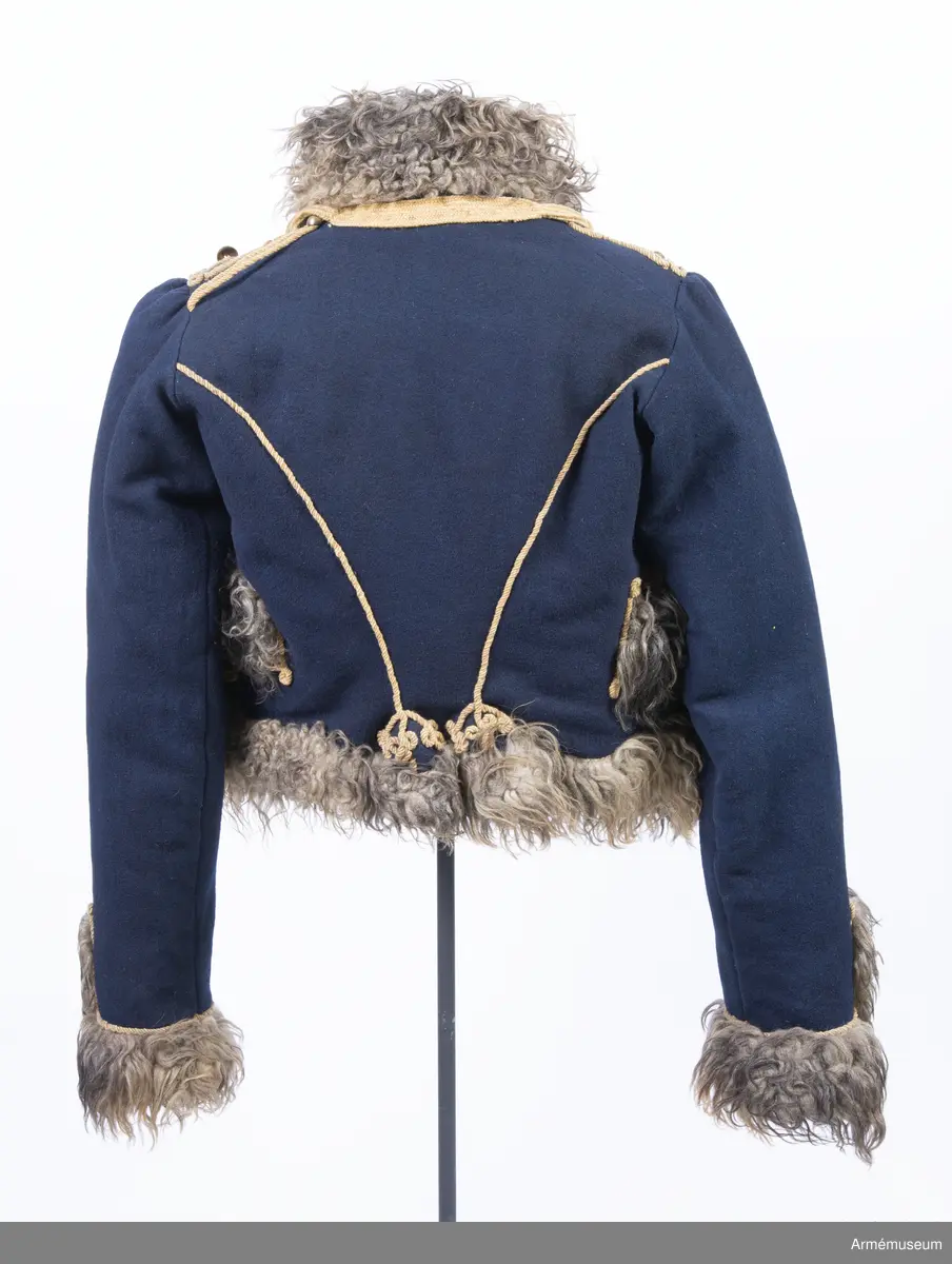 Blå päls med krage och ärmuppslag av gråbrunt fårskinn, med snören av gult ullgarn.

Pälsen är sydd av mörkblått kläde och är helfodrad med vitt, numera gulnat, korthårigt fårskinn. Ärmar, krage, framkanter och nederkant har bräm av gråbrunt fårskinn med lång lugg.
Plagget är konstruerat med fram- och sidstycken i ett samt helt bakstycke med litet skört i sidsömmarna. Ärmarna är ensömsärmar eller S-ärmar.
Tvärs över bröstet löper 18 rader snörmakerier gjorda av gul löst spunnen tvåtrådig ullsnodd. 5 knapprader, varav de två yttersta på varje sida har kullriga knappar medan knappraden i mitten som är avsedd att knäppas har klotknappar. Samtliga knappar är gjorda i en mässingslegering.
Ärmarna är kantade med päls. Pälsbrämet går upp i en "ruta" på framärmen, kantad med snodd. På baksidan av plagget nertill under ärmarna sitter två separata "rutor" av päls kantad med snodd. Sidsömmarna bak är markerade med snoddar som också pryder skörtets veck.
På baksidan av plagget nedanför kragen är det fäst ett flätat hängsle vars ändar hänger ner från varje axel och fram till plaggets främre nederkant. Varje del av hängslet är avslutat i en tofs. Vänster hängsle har ett spolformat knäppe klädd med snörmakeriarbete, medan det högra har en knut. Dessa är avsedda att hålla ihop plagget när det hänger öppet över vänster axel.
På vänster axel sitter en axelträns av dubbel snodd som sätts fast med en mässingsknapp.