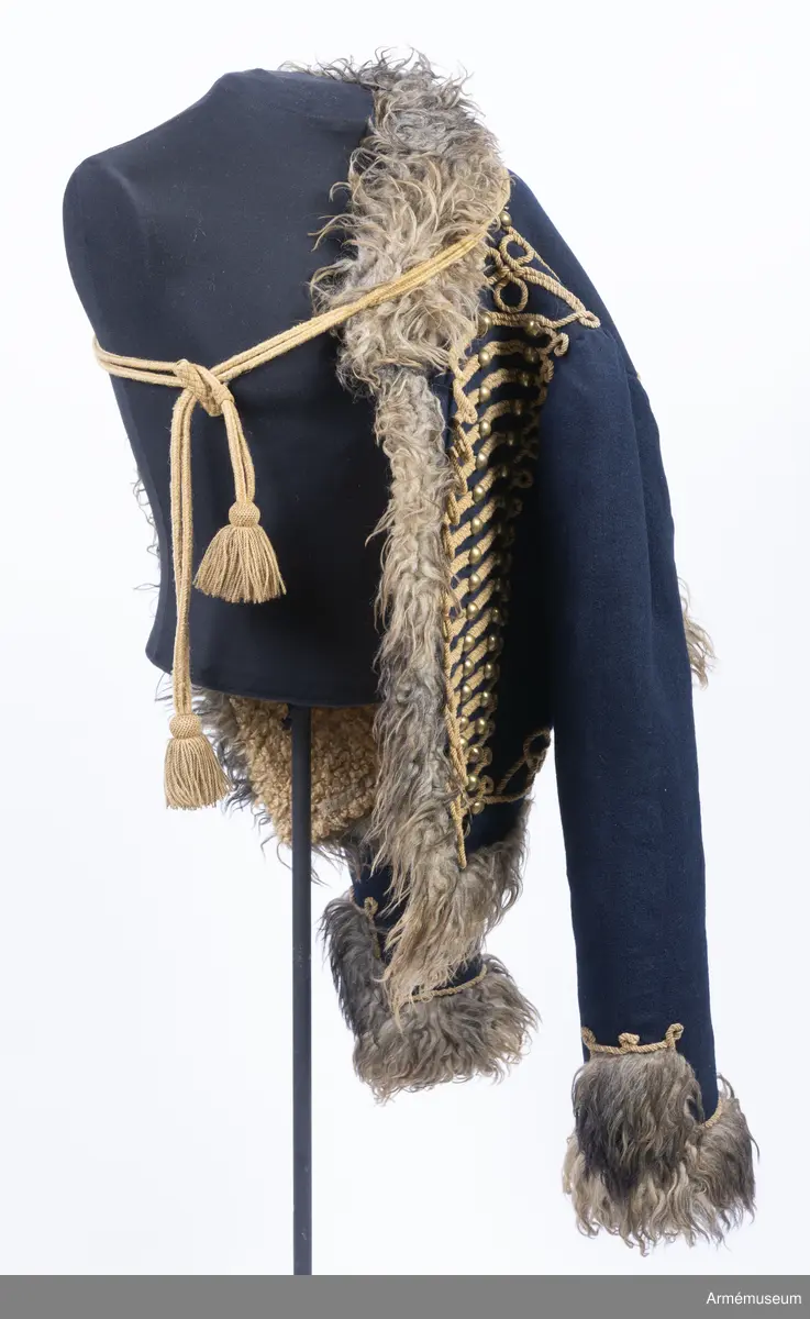 Blå päls med krage och ärmuppslag av gråbrunt fårskinn, med snören av gult ullgarn.

Pälsen är sydd av mörkblått kläde och är helfodrad med vitt, numera gulnat, korthårigt fårskinn. Ärmar, krage, framkanter och nederkant har bräm av gråbrunt fårskinn med lång lugg.
Plagget är konstruerat med fram- och sidstycken i ett samt helt bakstycke med litet skört i sidsömmarna. Ärmarna är ensömsärmar eller S-ärmar.
Tvärs över bröstet löper 18 rader snörmakerier gjorda av gul löst spunnen tvåtrådig ullsnodd. 5 knapprader, varav de två yttersta på varje sida har kullriga knappar medan knappraden i mitten som är avsedd att knäppas har klotknappar. Samtliga knappar är gjorda i en mässingslegering.
Ärmarna är kantade med päls. Pälsbrämet går upp i en "ruta" på framärmen, kantad med snodd. På baksidan av plagget nertill under ärmarna sitter två separata "rutor" av päls kantad med snodd. Sidsömmarna bak är markerade med snoddar som också pryder skörtets veck.
På baksidan av plagget nedanför kragen är det fäst ett flätat hängsle vars ändar hänger ner från varje axel och fram till plaggets främre nederkant. Varje del av hängslet är avslutat i en tofs. Vänster hängsle har ett spolformat knäppe klädd med snörmakeriarbete, medan det högra har en knut. Dessa är avsedda att hålla ihop plagget när det hänger öppet över vänster axel.
På vänster axel sitter en axelträns av dubbel snodd som sätts fast med en mässingsknapp.