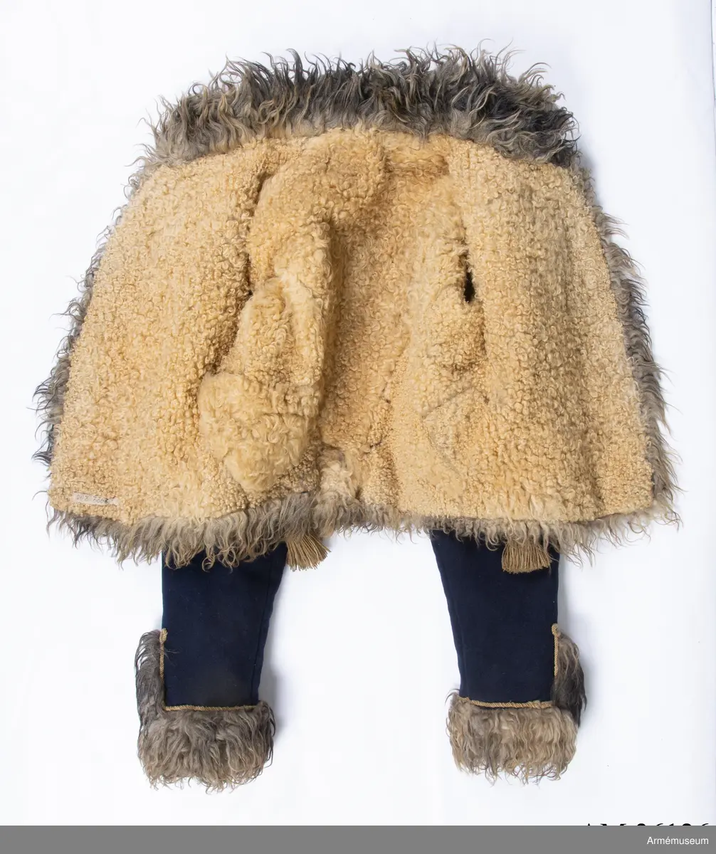 Blå päls med krage och ärmuppslag av gråbrunt fårskinn, med snören av gult ullgarn.

Pälsen är sydd av mörkblått kläde och är helfodrad med vitt, numera gulnat, korthårigt fårskinn. Ärmar, krage, framkanter och nederkant har bräm av gråbrunt fårskinn med lång lugg.
Plagget är konstruerat med fram- och sidstycken i ett samt helt bakstycke med litet skört i sidsömmarna. Ärmarna är ensömsärmar eller S-ärmar.
Tvärs över bröstet löper 18 rader snörmakerier gjorda av gul löst spunnen tvåtrådig ullsnodd. 5 knapprader, varav de två yttersta på varje sida har kullriga knappar medan knappraden i mitten som är avsedd att knäppas har klotknappar. Samtliga knappar är gjorda i en mässingslegering.
Ärmarna är kantade med päls. Pälsbrämet går upp i en "ruta" på framärmen, kantad med snodd. På baksidan av plagget nertill under ärmarna sitter två separata "rutor" av päls kantad med snodd. Sidsömmarna bak är markerade med snoddar som också pryder skörtets veck.
På baksidan av plagget nedanför kragen är det fäst ett flätat hängsle vars ändar hänger ner från varje axel och fram till plaggets främre nederkant. Varje del av hängslet är avslutat i en tofs. Vänster hängsle har ett spolformat knäppe klädd med snörmakeriarbete, medan det högra har en knut. Dessa är avsedda att hålla ihop plagget när det hänger öppet över vänster axel.
På vänster axel sitter en axelträns av dubbel snodd som sätts fast med en mässingsknapp.