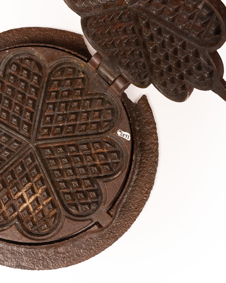 Kakejern for vafler produsert i støpejern. Jernet lager vafler med fem hjerter. Jernet er tilpasset ringkomfyren og har en ramme rundt som settes på kanten av hulle i komfyren. Jernet kan snus 180 grader rundt sin egen akse ved hjelp av to sylindere som hviler på spor i rammen.  

Jernet åpnes ved hjelp av et håndtak festet i en av endene på oversiden av lokket. På motsatt side er det et en hengsel som fester over og undersiden av jernet sammen. På lokket er det også støpt inn en oppskrift på vafler. Rammen til jernet har et håndtak i ene enden. På motsatt side er det en tydelig skade i rammen som tilsier at det har vært et identisk håndbak også her. 

Jernet viser tydelige tegn på rust grunnet oksidering. 