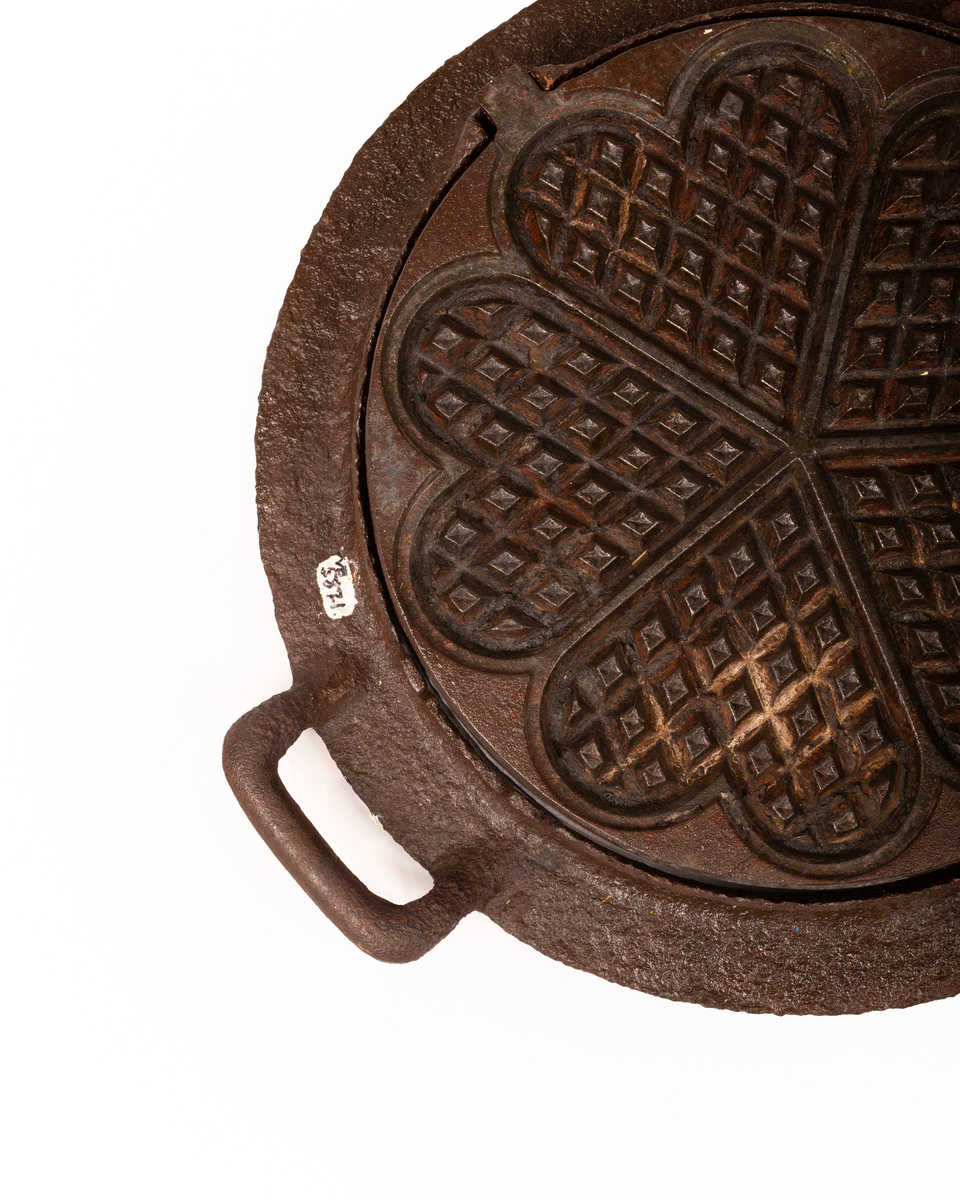 Kakejern for vafler produsert i støpejern. Jernet lager vafler med fem hjerter. Jernet er tilpasset ringkomfyren og har en ramme rundt som settes på kanten av hulle i komfyren. Jernet kan snus 180 grader rundt sin egen akse ved hjelp av to sylindere som hviler på spor i rammen.  

Jernet åpnes ved hjelp av et håndtak festet i en av endene på oversiden av lokket. På motsatt side er det et en hengsel som fester over og undersiden av jernet sammen. På lokket er det også støpt inn en oppskrift på vafler. Rammen til jernet har et håndtak i ene enden. På motsatt side er det en tydelig skade i rammen som tilsier at det har vært et identisk håndbak også her. 

Jernet viser tydelige tegn på rust grunnet oksidering. 