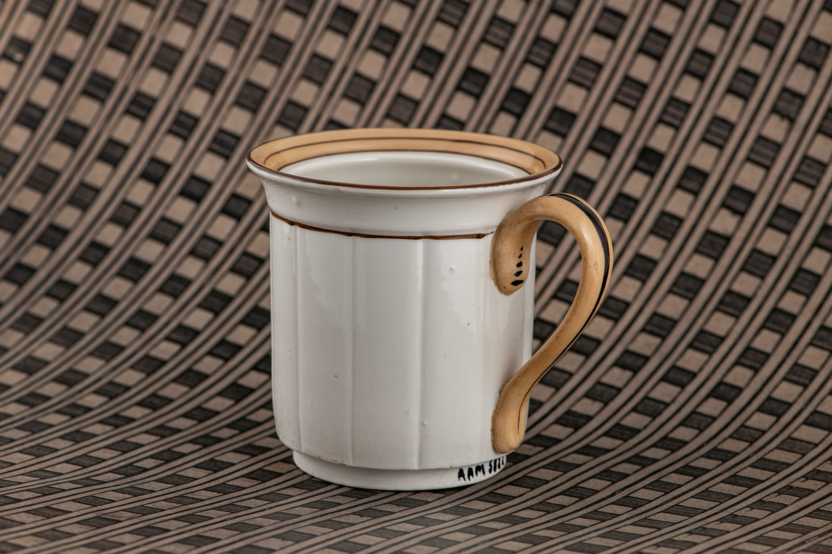 Tetrakter eller kaffetrakter formet som et krus. Umerket. Hvitt porselen med brunt dekor. Rette sider med vertikale riller, utbøyd munningsrand dekorert med brune ringer og et belte av lysbrun glasur. Rundet lysbrun hank med mørkebrun stripe. Tetthullet uglasert bunn.
