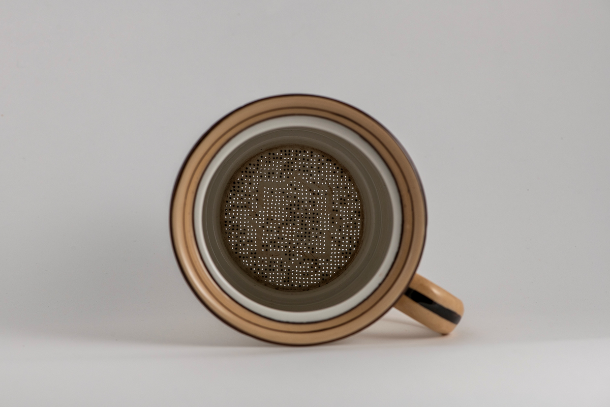 Tetrakter eller kaffetrakter formet som et krus. Umerket. Hvitt porselen med brunt dekor. Rette sider med vertikale riller, utbøyd munningsrand dekorert med brune ringer og et belte av lysbrun glasur. Rundet lysbrun hank med mørkebrun stripe. Tetthullet uglasert bunn.
