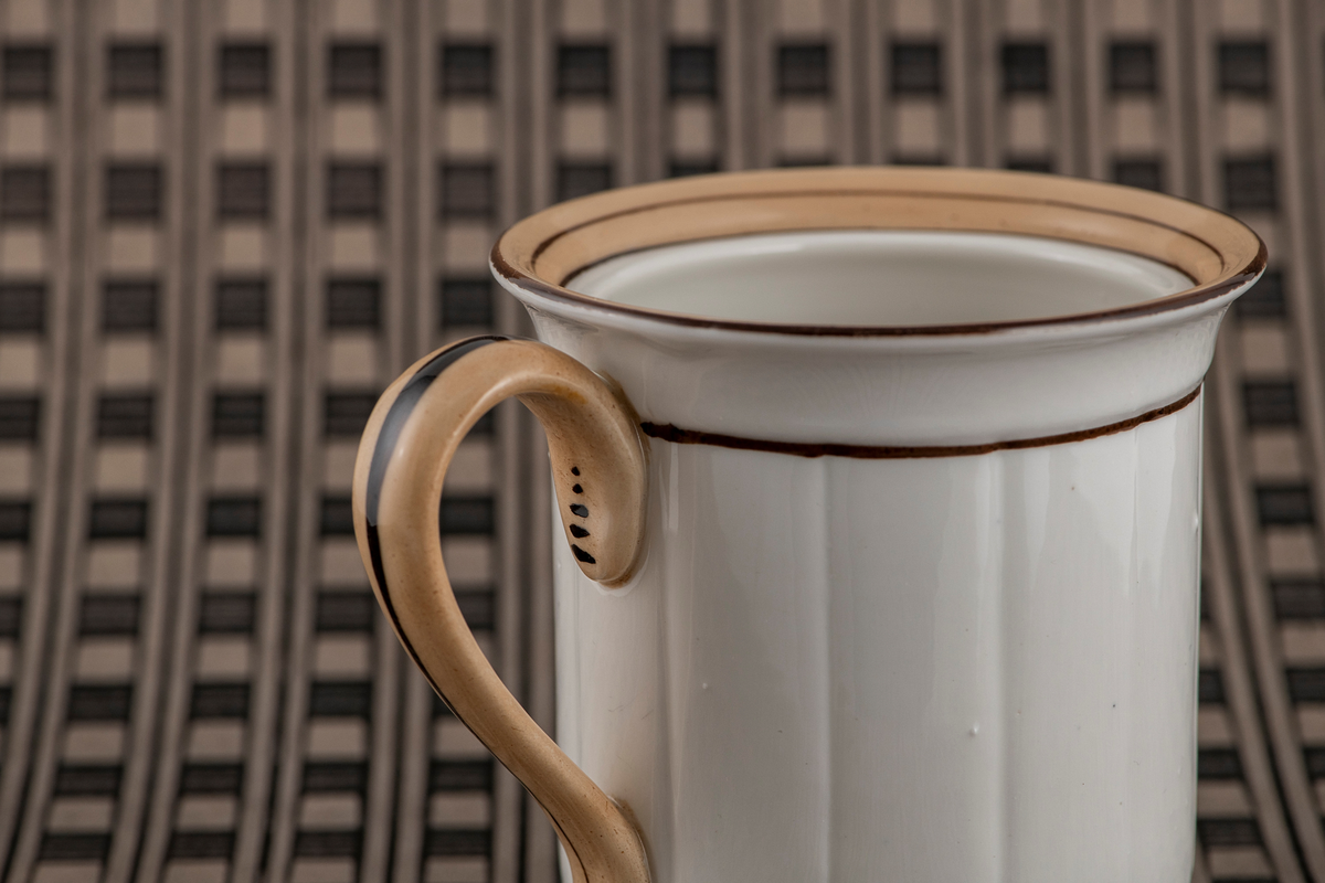 Tetrakter eller kaffetrakter formet som et krus. Umerket. Hvitt porselen med brunt dekor. Rette sider med vertikale riller, utbøyd munningsrand dekorert med brune ringer og et belte av lysbrun glasur. Rundet lysbrun hank med mørkebrun stripe. Tetthullet uglasert bunn.
