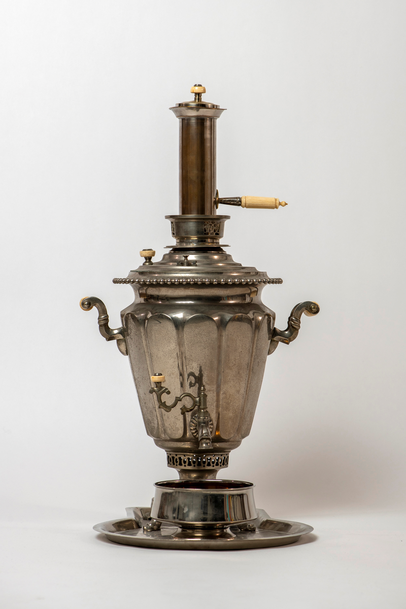 Samovar. Rund fot på fire utskrånende føtter. Stett med gjennombrutt dekor. Korpus med sider med rifler og avlange fasetter. To runde, tverr-riflede hanker av ben. Profilert overstykke med to benknotter. Ovalt fabrikkmerke med russisk tekst. Toppstykke med tre gjennombrutte ornamenter, nedsenket tungt lokk med ben-knott. Kran nederst på korpus, åpning i bunnen, og liten åpning for damp på overstykket.

Pipe. Forkrommet, skaft av messing og ben. Høy sylinderformet med utskrådd fotstykke, uten bunn, stjerthank.

Dryppskål av messing, utvendig forkrommet. Skål på stett. Midt i bunnen innvendig er det et ovalt firmamerke med russisk tekst.

Brett av forkrommet messing. Firkantet smal del, den annen halvdel bredere med rundet kontur.