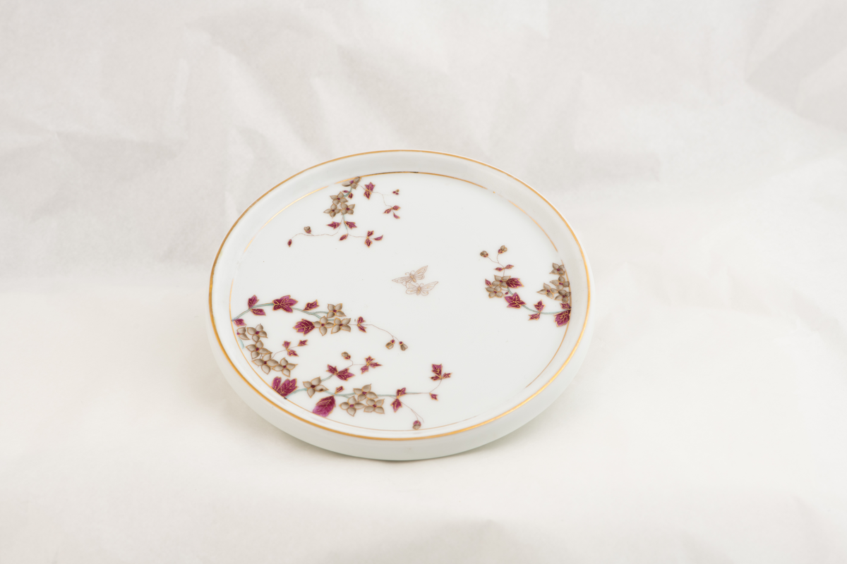 En porselenstallerken med påmalte blomster og to sommerfugler.