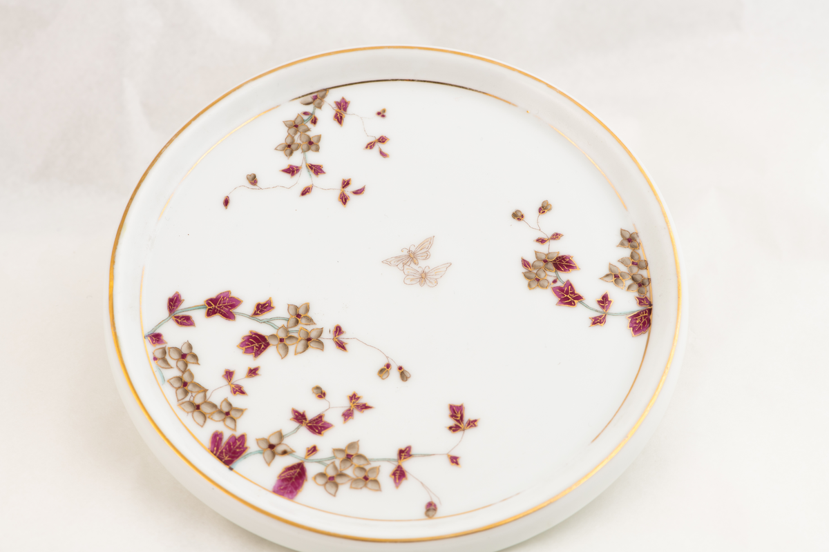 En porselenstallerken med påmalte blomster og to sommerfugler.