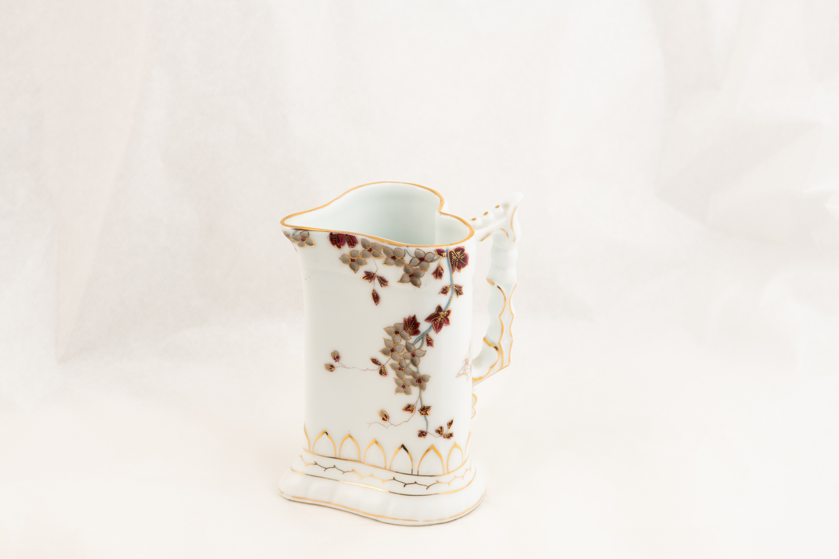 En hjerteformet porselenskanne med påmalte blomster og sommerfugler.