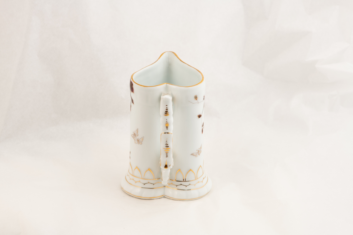 En hjerteformet porselenskanne med påmalte blomster og sommerfugler.