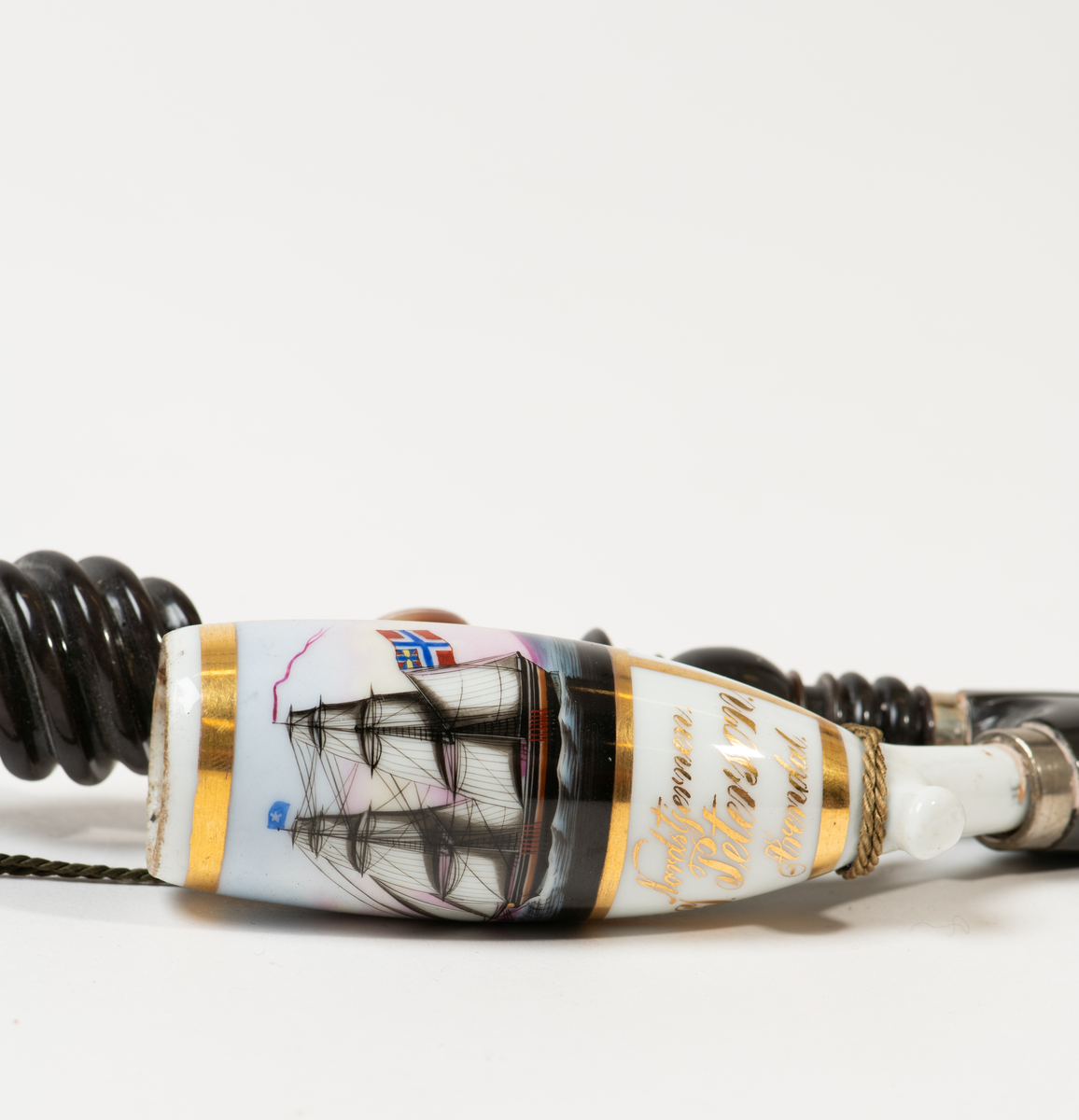 Lang pipe med tilknytning til Merdøgaard og Larssønfamilien. Pipen består av mange ulike materialer og har et stort pipehode i porselen. Pipehodet er dekorert med et lite maleri av skipet Nordstjernen med det norske flagg i masta med unionsmerket med det svenske flagget i det ene hjørnet, også kalt "sildesalaten". Slike flagg var vanlige før unionsoppløsningen i 1905. Rundt maleriet er det malt med streker med gullmaling. Under maleriet står det "Nordstjernen.", "J. Peterson." og "Arendal". Pipeskaftet består av mange materialer som horn/bein som er dreid og utskåret på en dekorativ måte som stikker ut.  Mot midten av pipen er det en skive av horn før pipeskaftet fortsetter opp mot munnstykket i et rør av metall og tekstil.  Ved munnstykket henger den en fargerik dusk og det er festet en snor som går dobbelt fra toppen av pipen og ned til pipehodet. Pipen har noen skader og var fortsatt full av tobakk da den ble registrert.