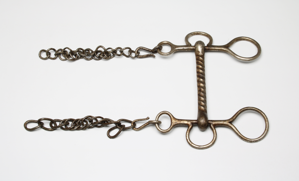 Kraftigt stångbett med räfflad stång. Parerstång med remöglor och tömringar. Kindkedja avbruten på mitten.