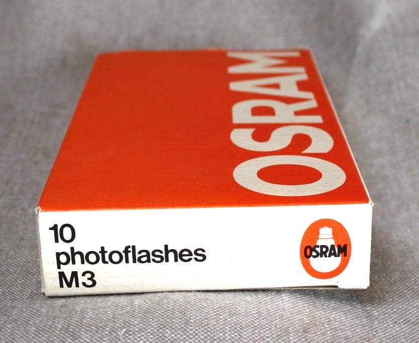 Pappeske med Osram blitzpærer, type Vacublitz M3. Pakken er åpnet og inneholder 5 pærer. Baksiden av pakken viser en rekke sjemaer med bruksområder og advarseler.
