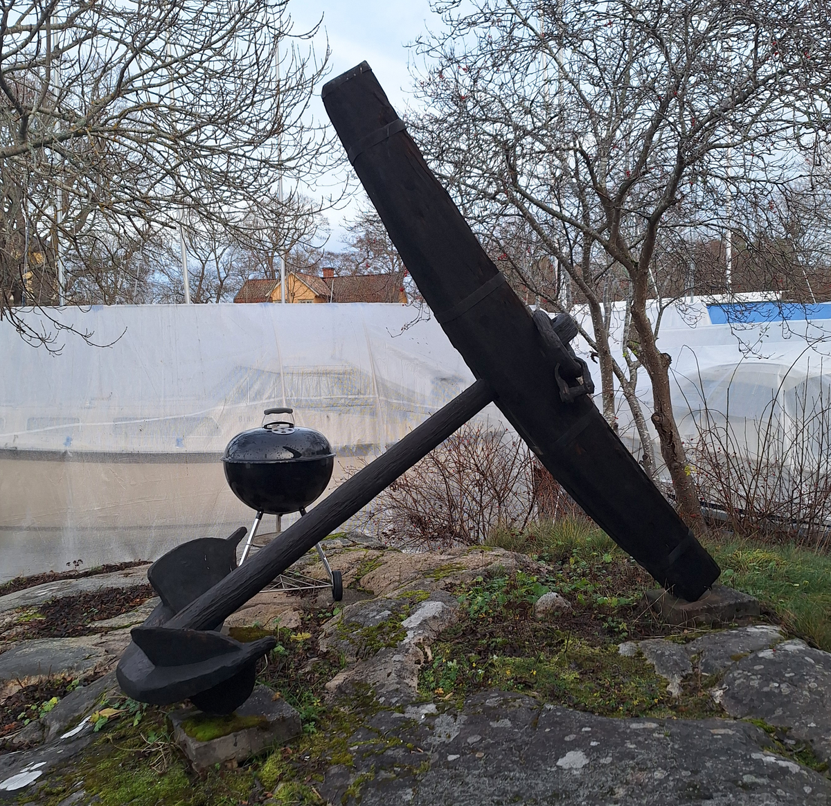 Stockankare. Trästock med fyra järnband samt en skyddskåpa i metall över ändträet på övre delen. Stockens två delar hålls ihop med fyra kilade trädymlingar. Stocken är på vissa partier mycket sliten. Schackel i röringen.