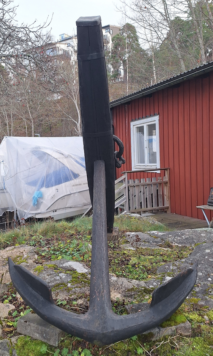 Stockankare. Trästock med fyra järnband samt en skyddskåpa i metall över ändträet på övre delen. Stockens två delar hålls ihop med fyra kilade trädymlingar. Stocken är på vissa partier mycket sliten. Schackel i röringen.