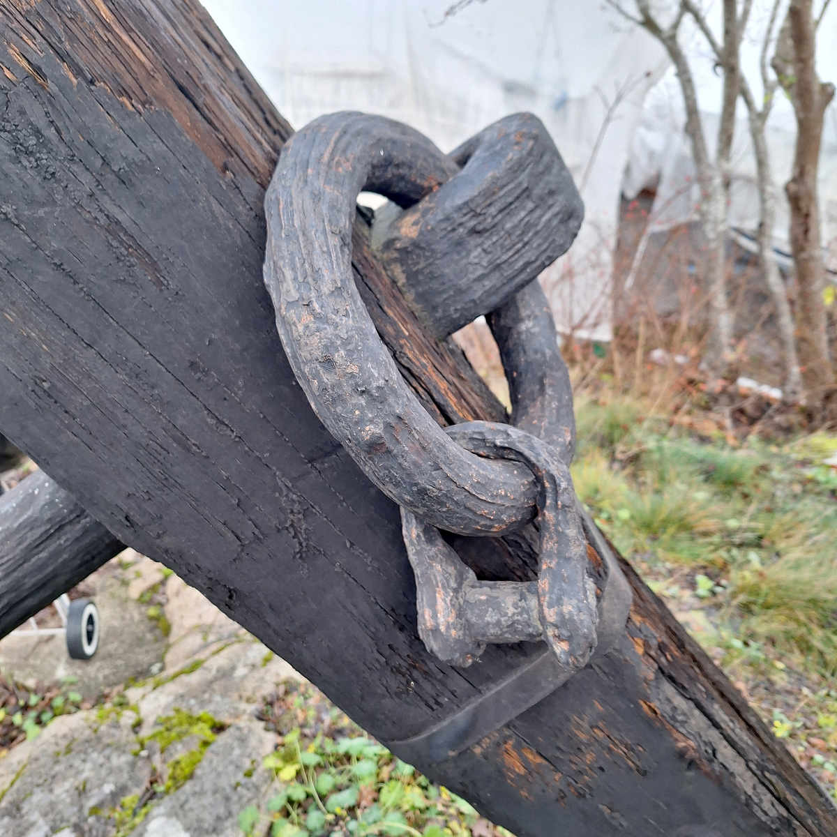 Stockankare. Trästock med fyra järnband samt en skyddskåpa i metall över ändträet på övre delen. Stockens två delar hålls ihop med fyra kilade trädymlingar. Stocken är på vissa partier mycket sliten. Schackel i röringen.