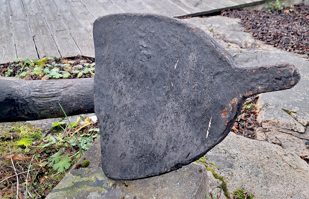Stockankare. Trästock med fyra järnband samt en skyddskåpa i metall över ändträet på övre delen. Stockens två delar hålls ihop med fyra kilade trädymlingar. Stocken är på vissa partier mycket sliten. Schackel i röringen.