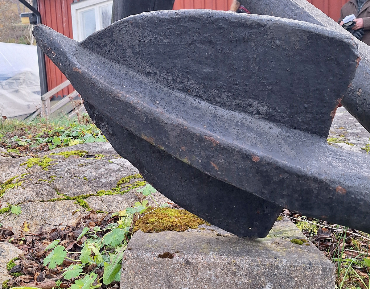 Stockankare. Trästock med fyra järnband samt en skyddskåpa i metall över ändträet på övre delen. Stockens två delar hålls ihop med fyra kilade trädymlingar. Stocken är på vissa partier mycket sliten. Schackel i röringen.