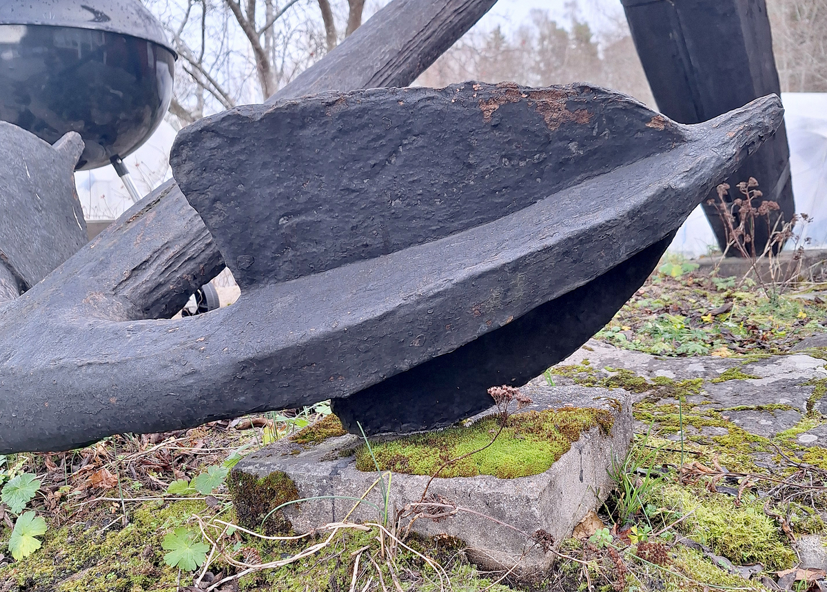 Stockankare. Trästock med fyra järnband samt en skyddskåpa i metall över ändträet på övre delen. Stockens två delar hålls ihop med fyra kilade trädymlingar. Stocken är på vissa partier mycket sliten. Schackel i röringen.