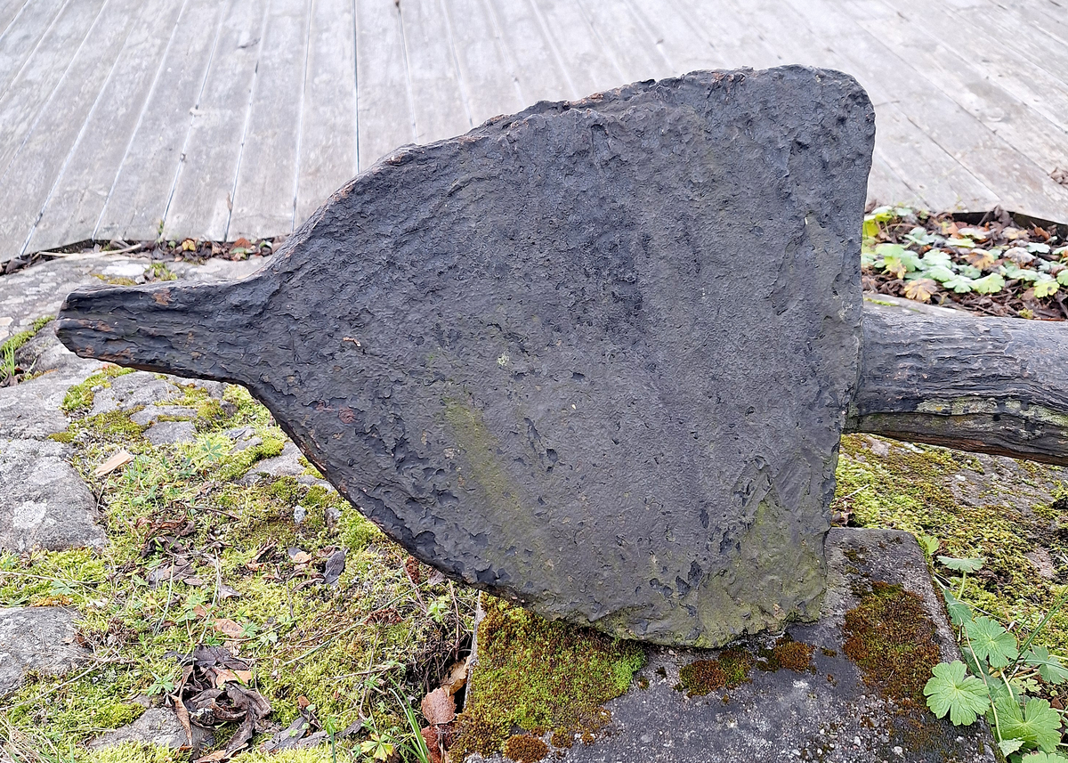 Stockankare. Trästock med fyra järnband samt en skyddskåpa i metall över ändträet på övre delen. Stockens två delar hålls ihop med fyra kilade trädymlingar. Stocken är på vissa partier mycket sliten. Schackel i röringen.