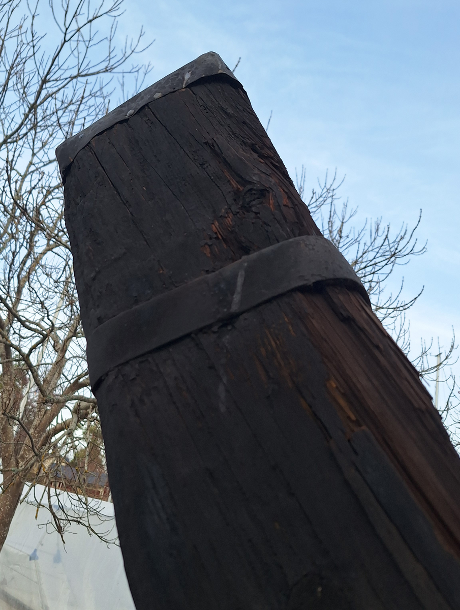 Stockankare. Trästock med fyra järnband samt en skyddskåpa i metall över ändträet på övre delen. Stockens två delar hålls ihop med fyra kilade trädymlingar. Stocken är på vissa partier mycket sliten. Schackel i röringen.