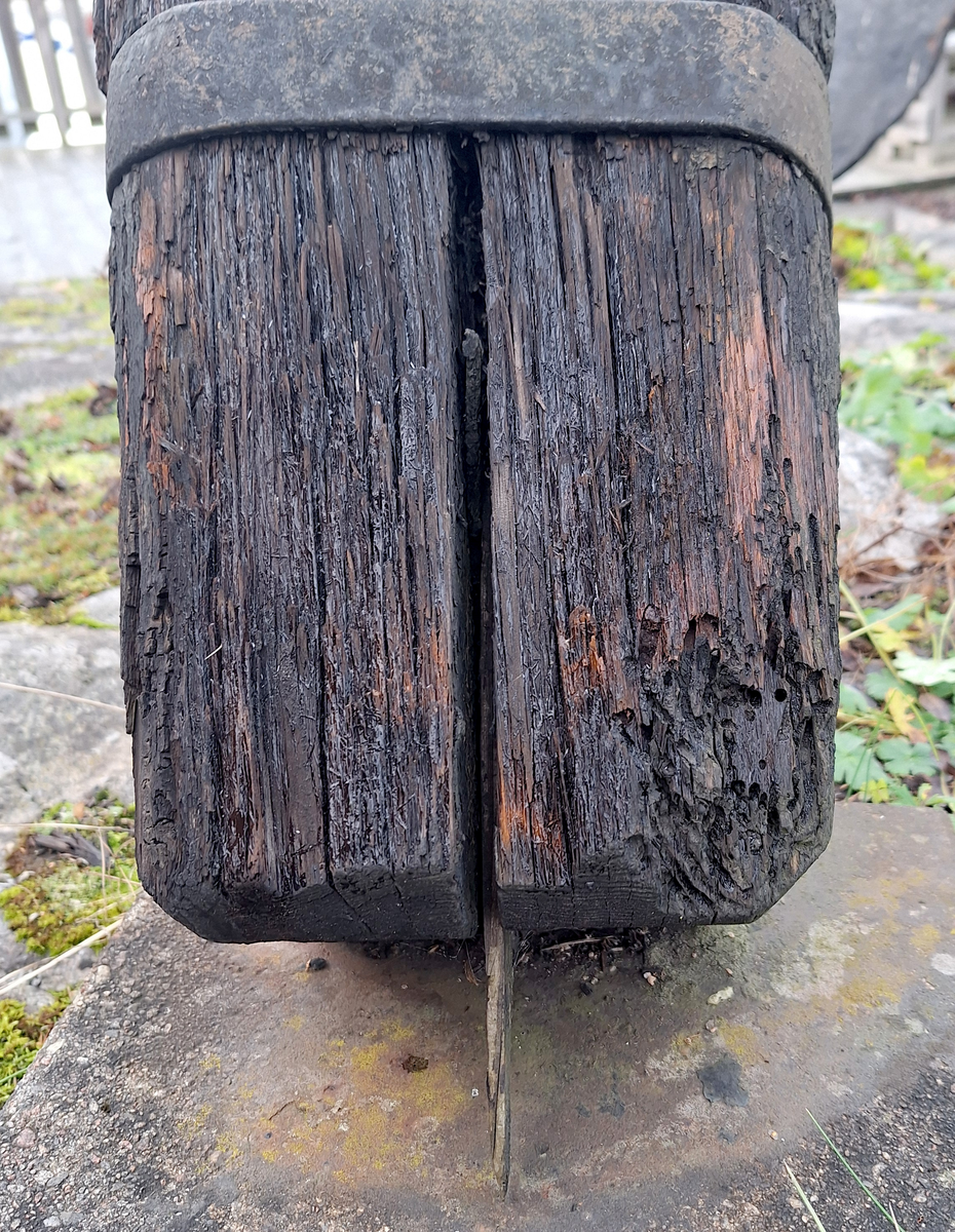 Stockankare. Trästock med fyra järnband samt en skyddskåpa i metall över ändträet på övre delen. Stockens två delar hålls ihop med fyra kilade trädymlingar. Stocken är på vissa partier mycket sliten. Schackel i röringen.