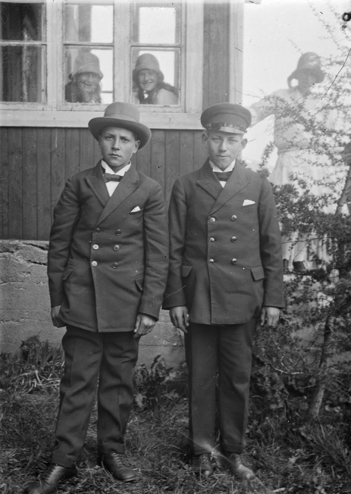 Leirfjord. To ukjente gutter i dress fotografert foran et hus. Tre ukjente jenter i bakgrunnen, to av disse innenfor et vindu.
