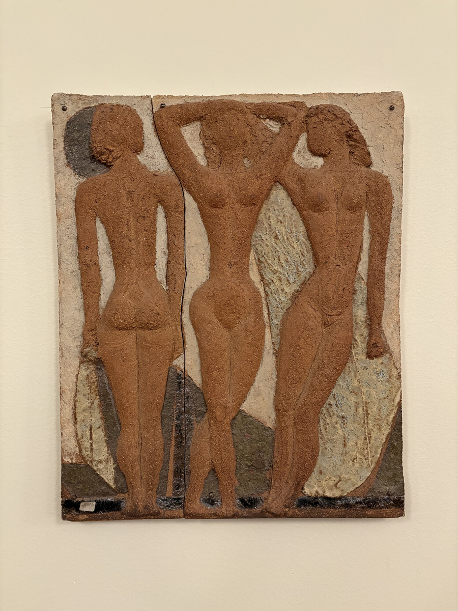 Tre Flickor, 1972, stengods. Motiv: Tre kvinnor, stående, i rödbrun kulör. Motivet i hög relief mot gulbeige botten. Reliefen består av två delar, monterade med skruv på en spånplatta. Konstnär: Tyra Lundgren. Mått: ca 51 x 43 cm. Tillstånd: 2017-11-20, Gott skick. 2018-01-31, Avsyning vid återlämning (se: Relationer/Relaterade lån) - Inget att tillägga / T.Å.
