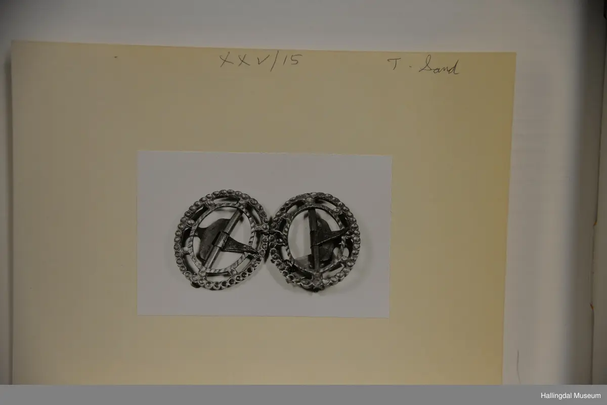 Oval spenne. Festet til skorne er av messing med ein tagg av jarn. Sjølve spennet er to ovale ringar, den eine noko mindre enn hin, som hekk saman av 8 mest kvadratiske stykke jamnt fordelt rundt ringane.